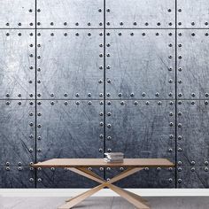 a table sitting in front of a metal wall with rivets on the side