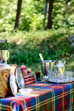 an outdoor picnic table set up with food and drinks on it, in the woods