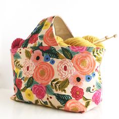 a flowered purse with yarn in it and knitting needles sticking out of the inside