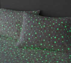 a bed with green stars on the sheets and pillowcases in front of a black headboard