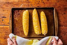 corn on the cob being peeled and placed on a baking sheet with napkins