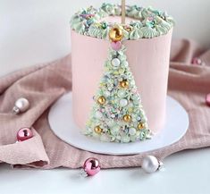 a pink cake decorated with a christmas tree on a white plate next to other decorations