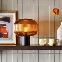 an orange flower sitting on top of a wooden shelf next to two cups and a vase