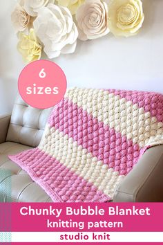 a pink and white crocheted blanket sitting on top of a couch next to flowers