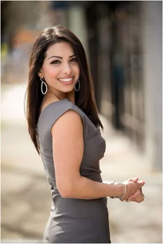 a woman in grey dress posing for the camera with her hand on her hip and smiling