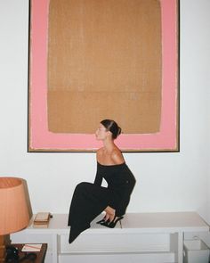 a woman sitting on top of a white table in front of a pink and brown painting