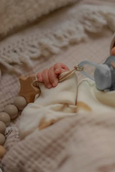 a baby laying on top of a bed next to a wooden beaded necklace and pacifier