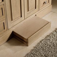 a wooden bench sitting in the middle of a room next to a rug and cabinets