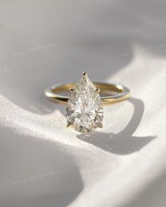 a yellow gold ring with a pear shaped diamond in the center on a white cloth