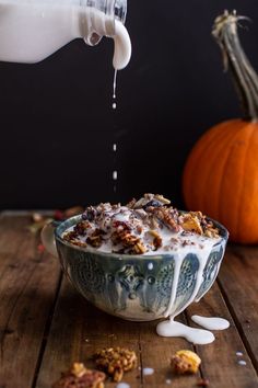 a person pouring milk into a bowl filled with granola, nuts and pumpkins