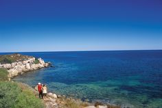 two people standing on the edge of a cliff looking out at the ocean