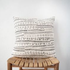 a white and black pillow sitting on top of a wooden chair next to a wall