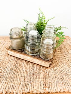 some jars are sitting on top of a wooden tray with plants in them and one is empty