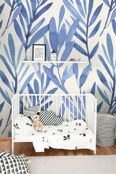 a white crib in front of a blue and white wall with leaves on it