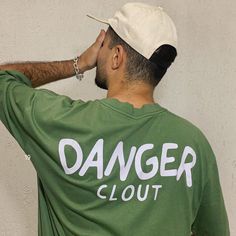 a man wearing a green shirt with the word danger clout printed on it and a white hat