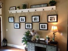 there are many pictures hanging on the wall above the desk and in front of it is a potted plant