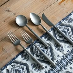 four forks and five spoons sitting on top of a tablecloth next to each other