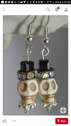 pair of skull earrings with crystal eyes and black top hats on them, hanging from hooks