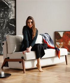 a woman sitting on top of a white couch in a living room next to a painting