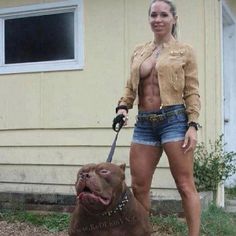 a woman standing next to a brown dog on a leash