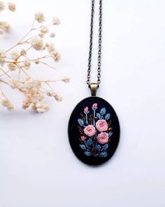 a black necklace with pink roses on it next to some dried flowers and a plant