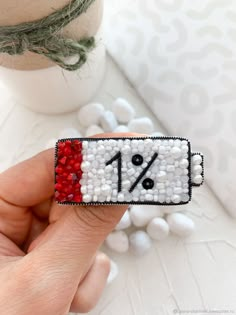 someone is holding a pin with the number one on it and beaded in red, white and black