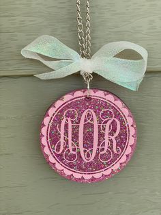 a pink necklace with a monogrammed initial on it and a bow hanging from the front