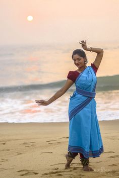 a woman standing on top of a sandy beach next to the ocean with her arms in the air