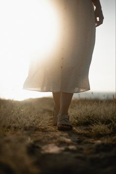 a woman in a white dress is walking towards the sun