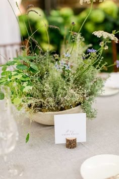 a table topped with lots of flowers and greenery on top of a white table cloth