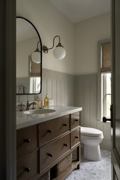 a white toilet sitting next to a bathroom sink under a large mirror on top of a wooden cabinet