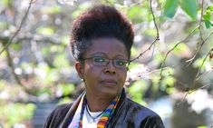 a woman with glasses standing in front of a tree and looking off into the distance