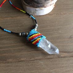 a beaded necklace with a crystal point on it sitting next to a potted plant