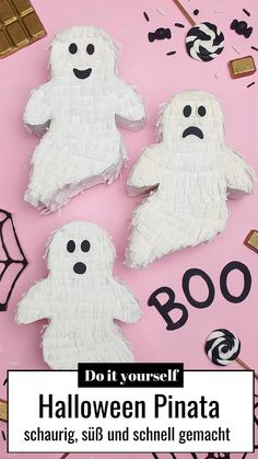 three white paper ghost pinatas sitting on top of a pink surface with black and white candies