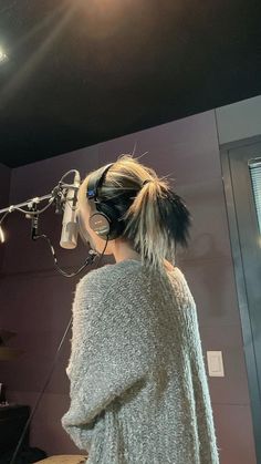 a woman wearing ear muffs standing in front of a microphone and recording equipment with headphones on her ears