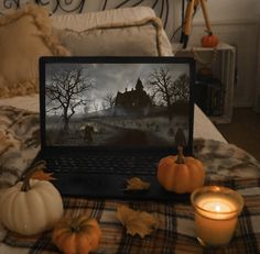 an open laptop computer sitting on top of a bed next to candles and pumpkins