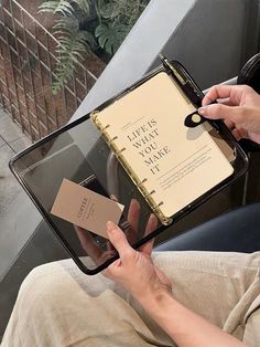 a person sitting down holding an open book with a notepad on top of it