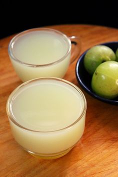 two glasses filled with liquid next to some green apples