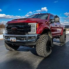 a large red truck parked on top of a parking lot next to snow covered ground