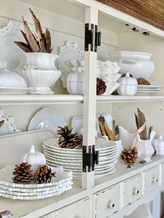 a white china cabinet filled with dishes and pine cones