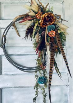 a wreath with feathers and flowers hanging on a door