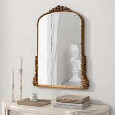 a mirror on the wall above a table with books and candles in front of it