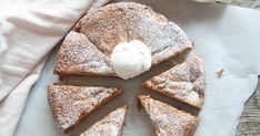 a piece of cake with powdered sugar on top is cut into eight pieces and sits on a napkin next to a cup of coffee