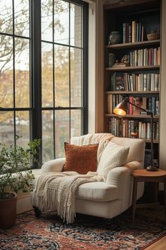 a white chair sitting in front of a window next to a book shelf filled with books