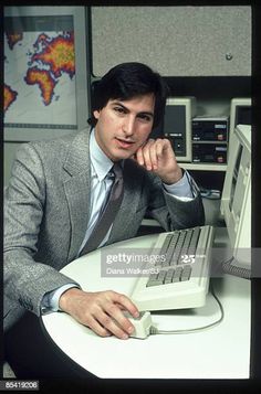 a man in a suit sitting at a desk with a computer monitor and keyboard on it