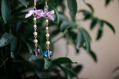 a pair of earrings hanging from a tree with purple ribbon and beads on it's end