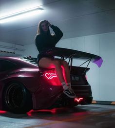 a woman sitting on top of a car in a parking garage with the hood up