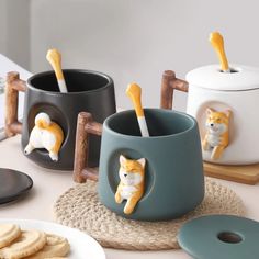 three coffee mugs with cats on them sitting on a table next to cookies and crackers