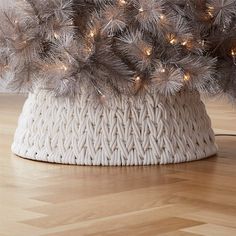 a white knitted basket with christmas lights on the top and silver tinseled branches