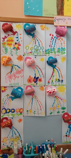 several colorful pictures on a bulletin board with pencils and crayons in front of them